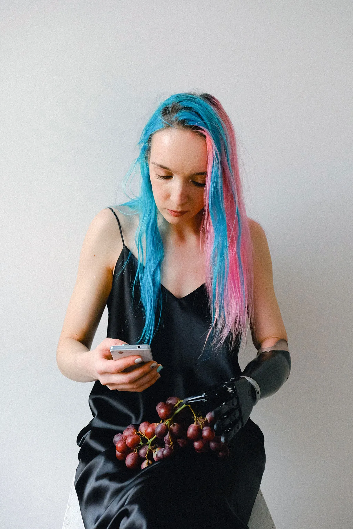 Frau mit pink-blauen Haaren hält Smartphone in Hand. Schwarze Prothese am rechten Unterarm.